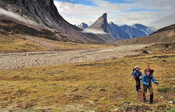 Zwei Wanderer durchqueren ein weites, felsiges Hochtal auf Baffin Island