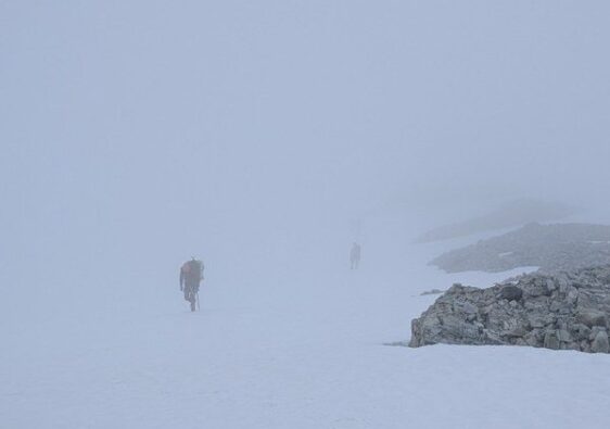 Bergsteiger bewegen sich bei dichtem Whiteout über einen verschneiten Gletscher