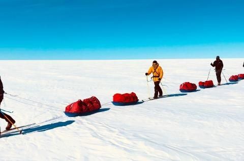 Expeditionsteilnehmer ziehen rote Pulken über eine verschneite Ebene